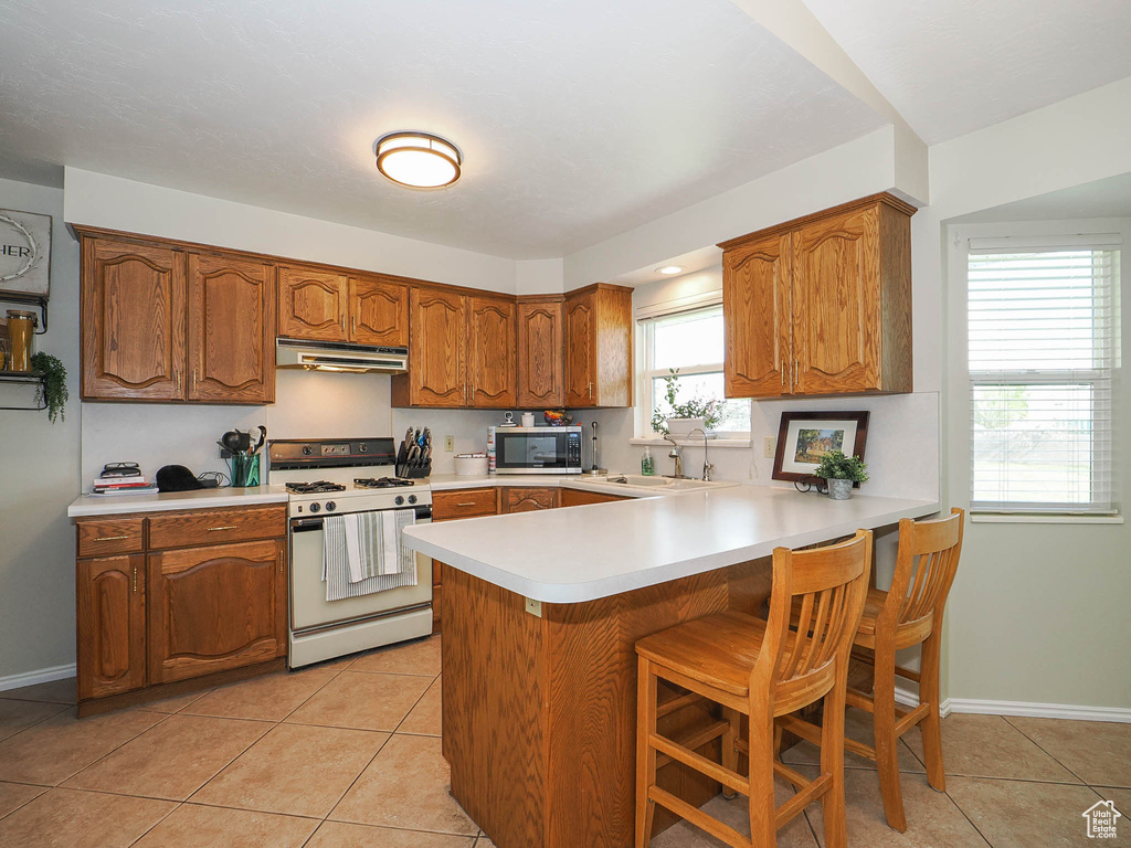 Kitchen with white gas stove, kitchen peninsula, a breakfast bar, and light tile flooring