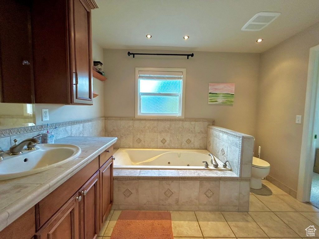 Bathroom featuring a relaxing tiled bath, vanity, tile floors, and toilet