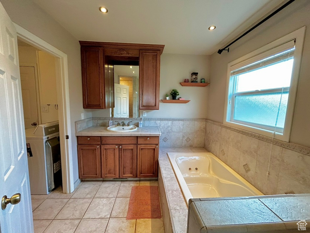 Bathroom with vanity with extensive cabinet space, washer / dryer, tile flooring, and tiled bath