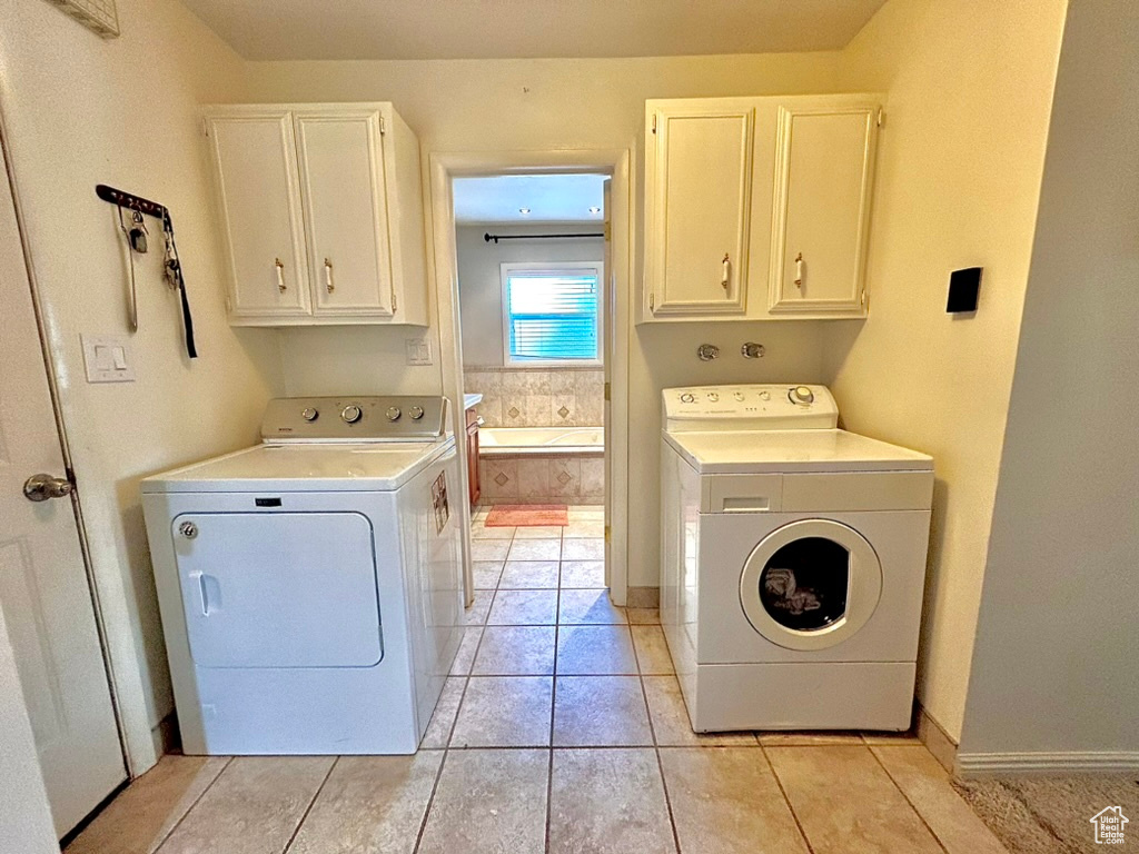 Clothes washing area featuring washing machine and dryer, cabinets, and light tile floors