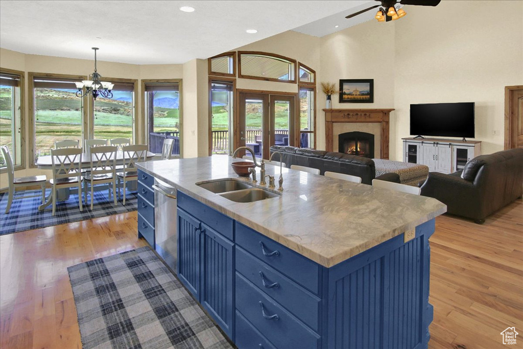 Kitchen with blue cabinetry, light hardwood / wood-style floors, ceiling fan with notable chandelier, an island with sink, and sink