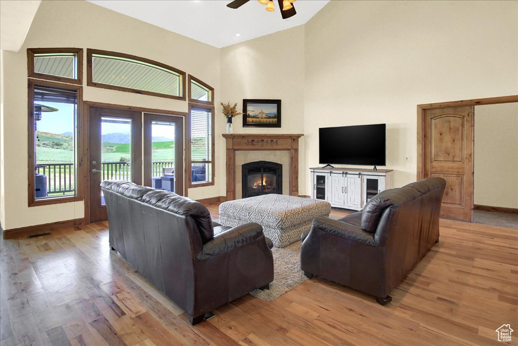 Living room with a towering ceiling, hardwood / wood-style floors, ceiling fan, and a tiled fireplace