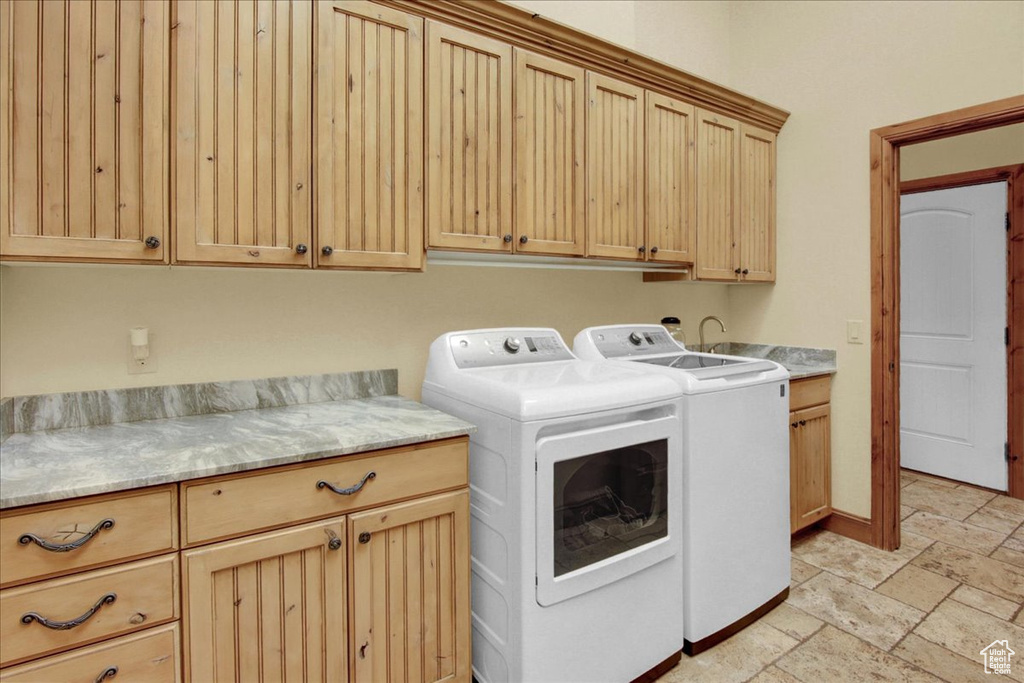 Clothes washing area with cabinets, light tile floors, and washer and dryer