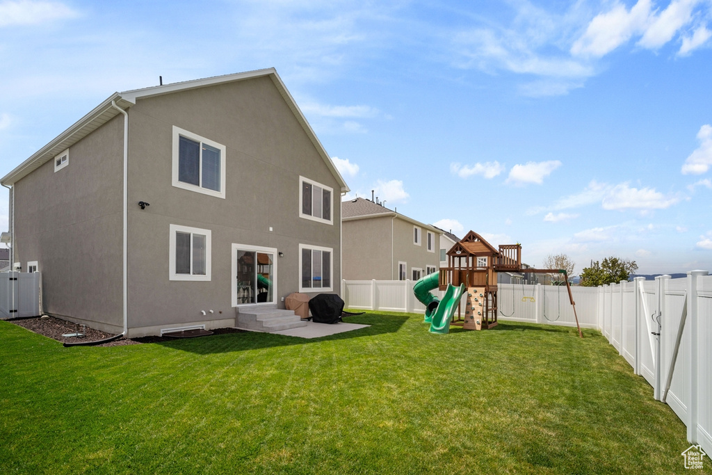 Rear view of property featuring a playground and a lawn