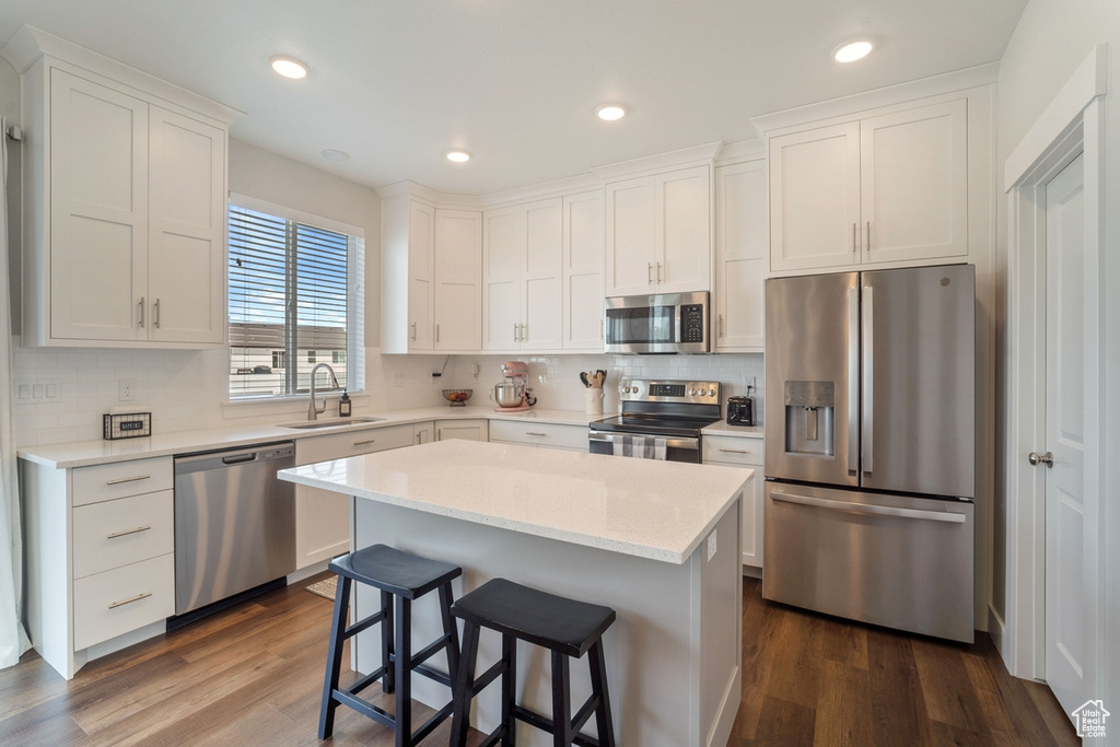 Kitchen featuring a kitchen island, sink, backsplash, dark wood-type flooring, and stainless steel appliances
