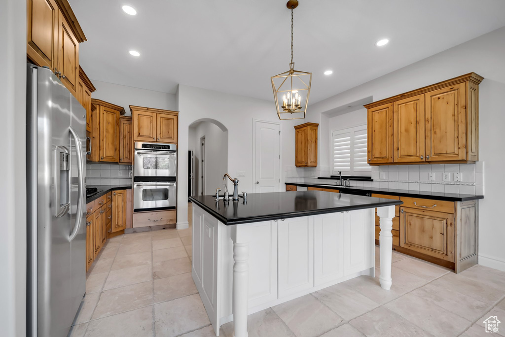 Kitchen with appliances with stainless steel finishes, light tile floors, sink, backsplash, and a kitchen island with sink