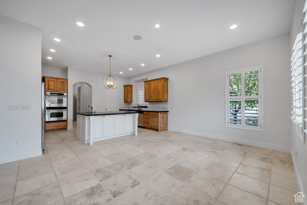 Kitchen featuring light tile floors, a kitchen island, tasteful backsplash, decorative light fixtures, and stainless steel double oven