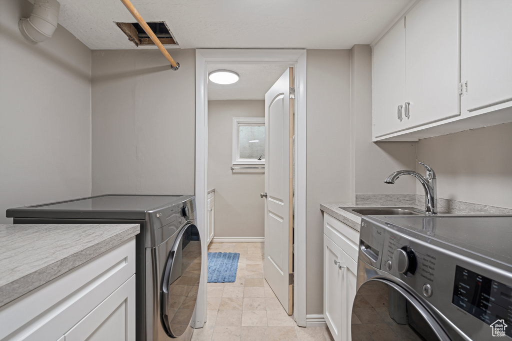 Washroom featuring washing machine and clothes dryer, cabinets, sink, and light tile flooring