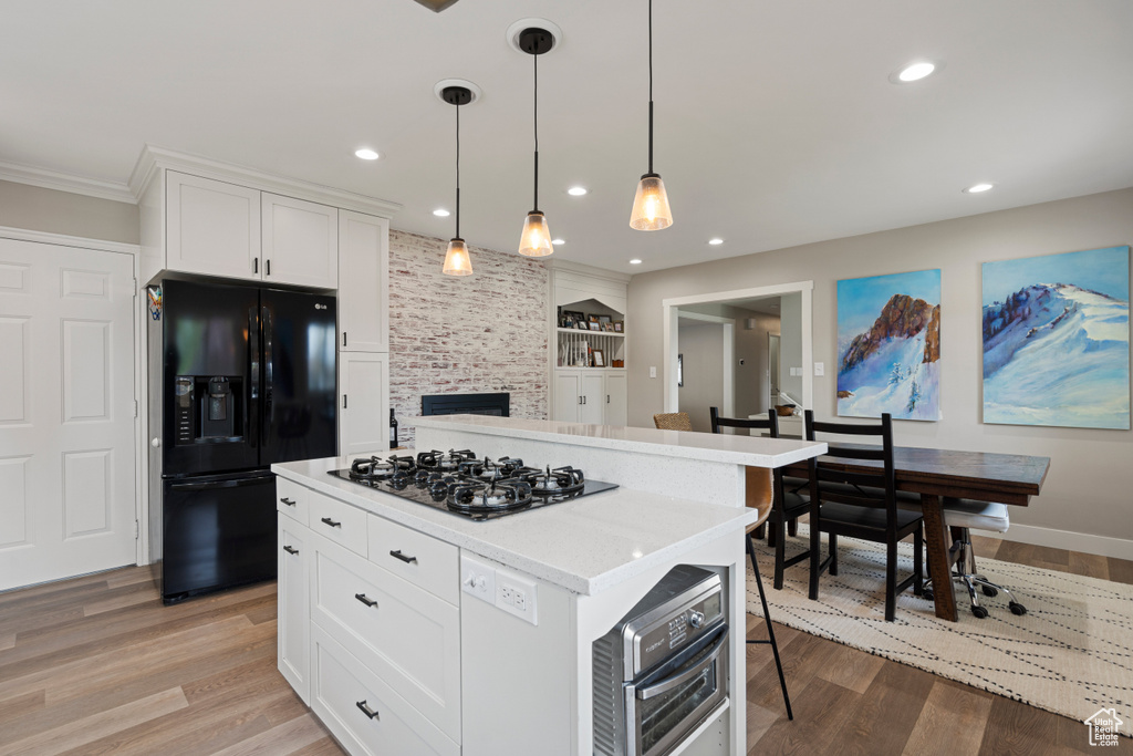 Kitchen with black fridge with ice dispenser, light hardwood / wood-style flooring, hanging light fixtures, and gas stovetop