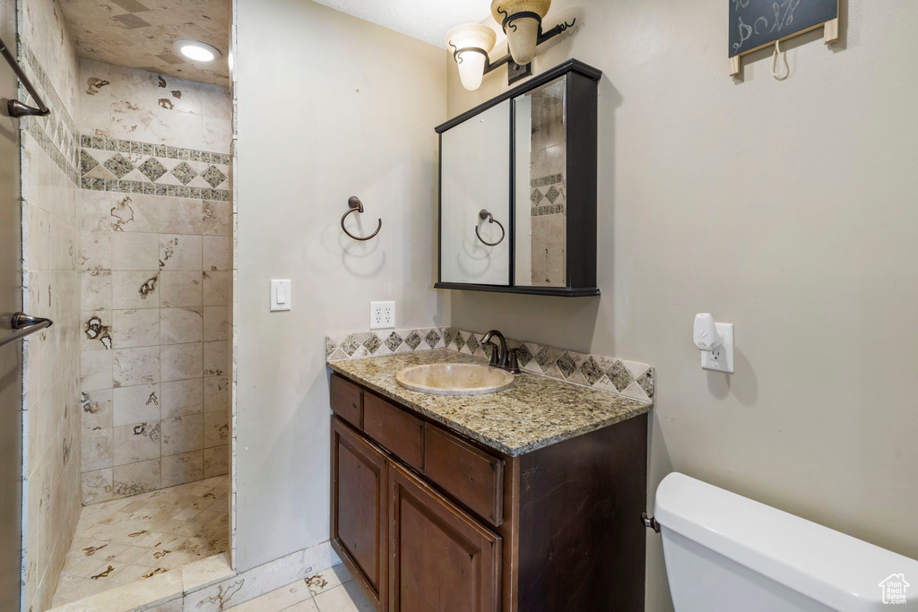 Bathroom featuring vanity, toilet, a tile shower, and tile flooring