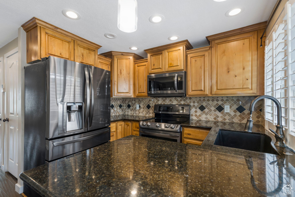 Kitchen with sink, appliances with stainless steel finishes, tasteful backsplash, and dark stone counters