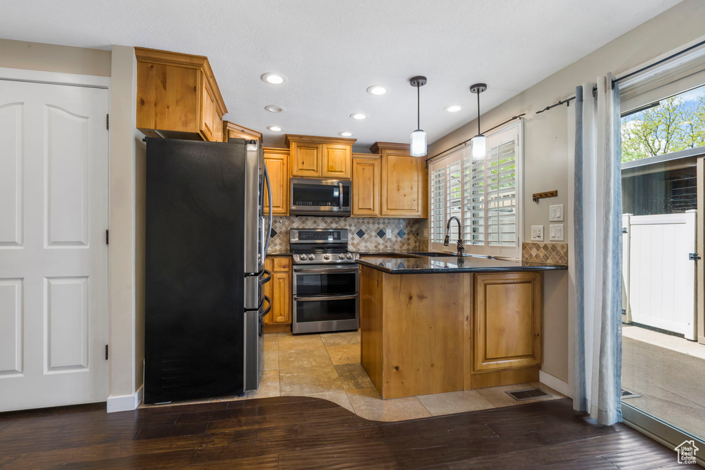 Kitchen with appliances with stainless steel finishes, backsplash, decorative light fixtures, light hardwood / wood-style flooring, and kitchen peninsula