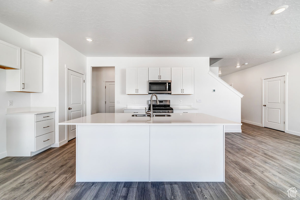 Kitchen with white cabinets, hardwood / wood-style floors, stainless steel appliances, and a center island with sink