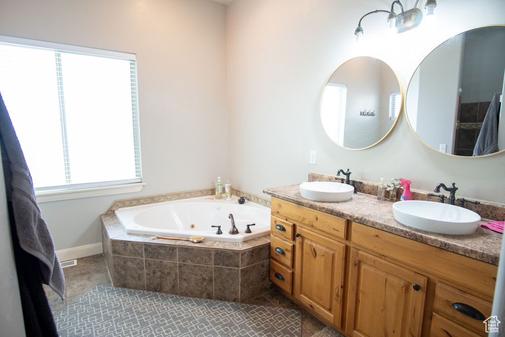 Bathroom with vanity with extensive cabinet space, dual sinks, tile flooring, and tiled bath