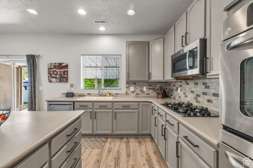 Kitchen with sink, stainless steel appliances, tasteful backsplash, gray cabinetry, and light wood-type flooring