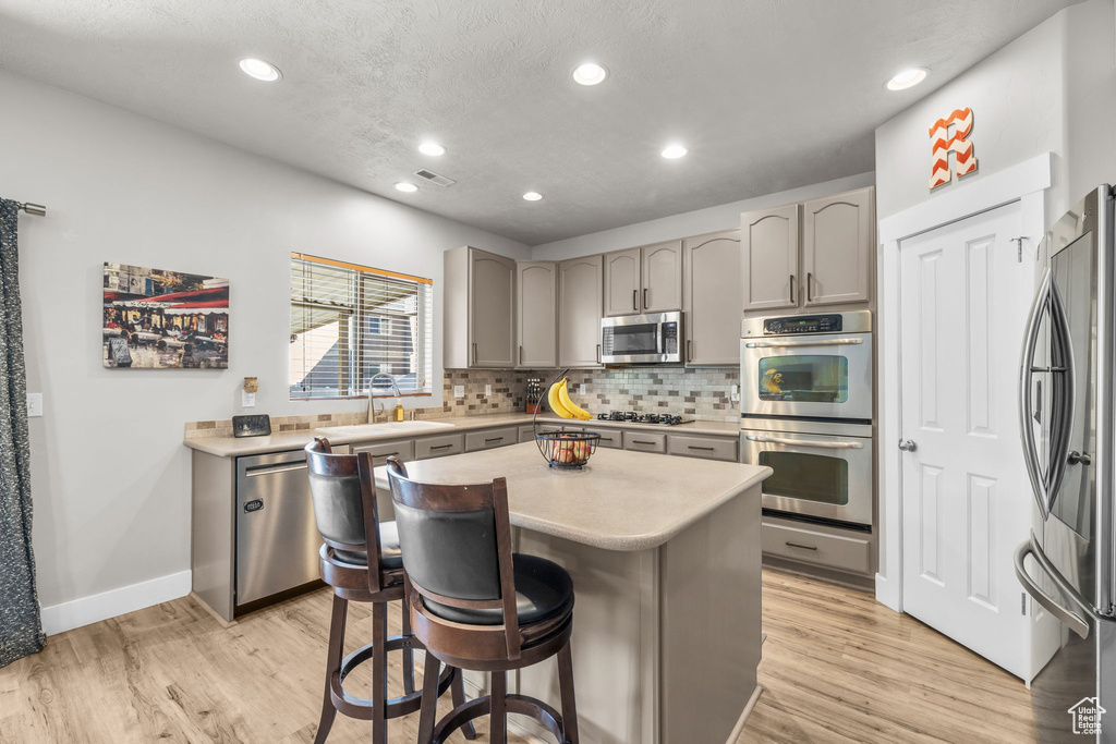 Kitchen featuring appliances with stainless steel finishes, light hardwood / wood-style flooring, gray cabinets, sink, and a center island