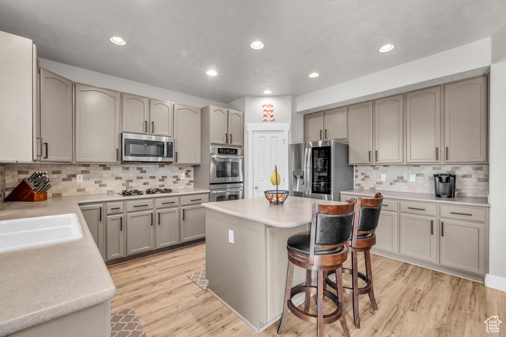 Kitchen with light hardwood / wood-style flooring, backsplash, appliances with stainless steel finishes, a kitchen bar, and a kitchen island