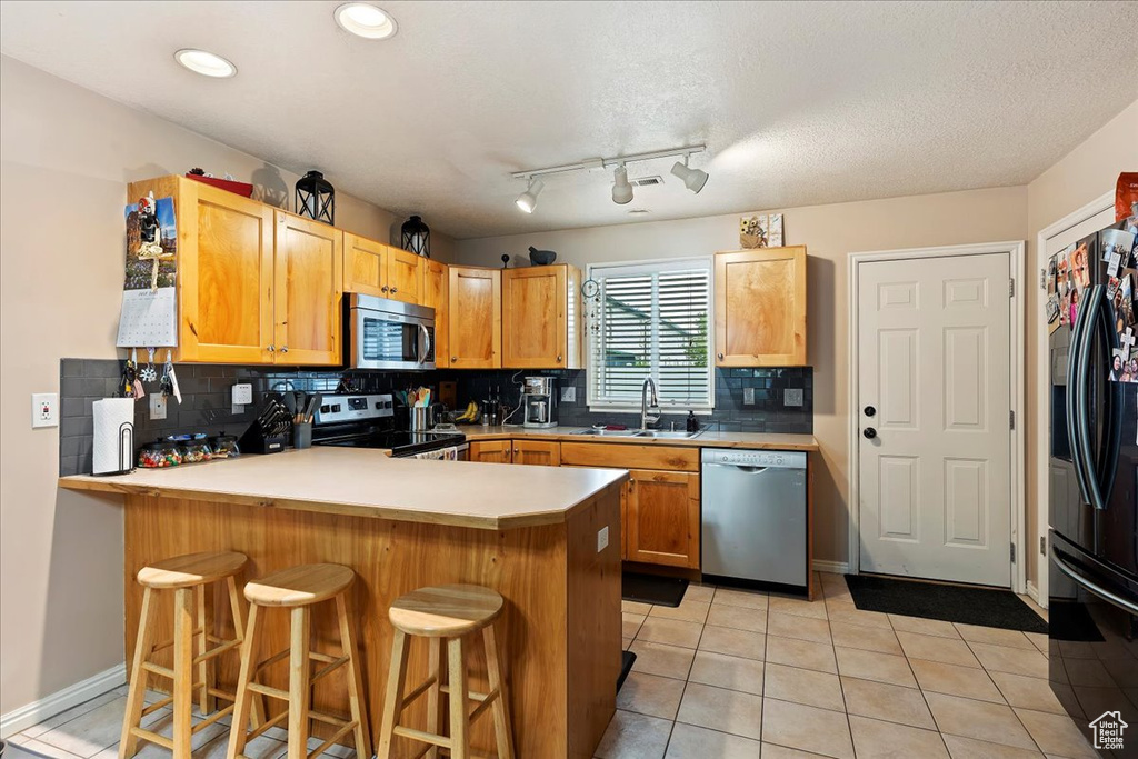 Kitchen with appliances with stainless steel finishes, light tile floors, sink, backsplash, and kitchen peninsula