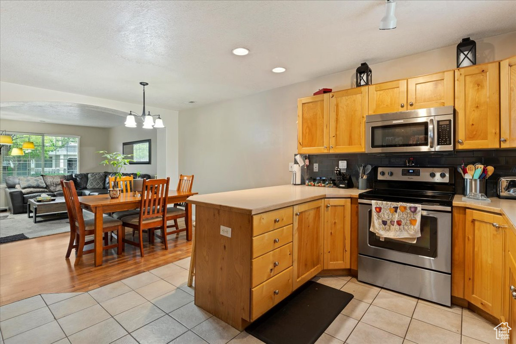 Kitchen with appliances with stainless steel finishes, tasteful backsplash, light wood-type flooring, and kitchen peninsula