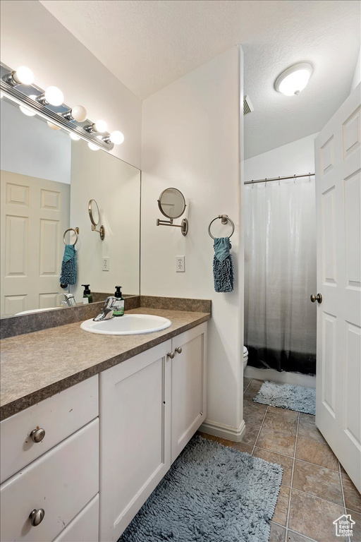 Bathroom with a textured ceiling, vanity, toilet, and tile flooring