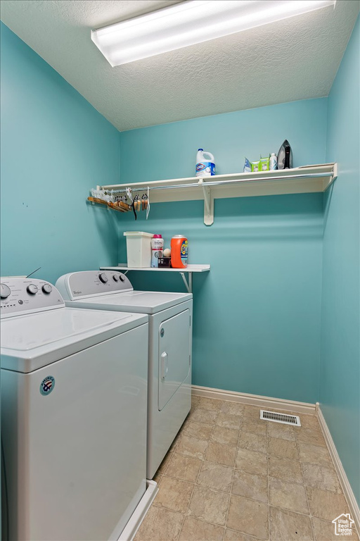 Laundry area with a textured ceiling, light tile floors, and washing machine and clothes dryer