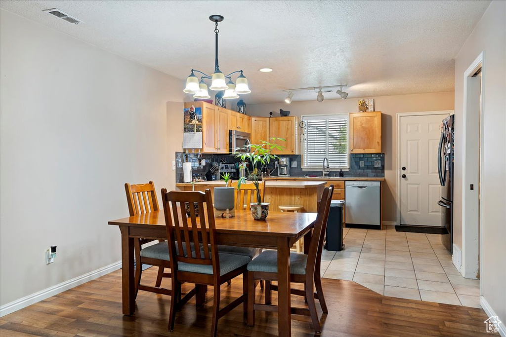 Dining room with light tile flooring, rail lighting, an inviting chandelier, sink, and a textured ceiling