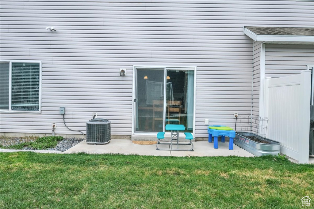 View of exterior entry with a patio, a lawn, and central air condition unit