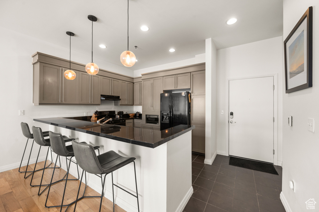 Kitchen featuring dark tile flooring, a breakfast bar area, black appliances, kitchen peninsula, and pendant lighting