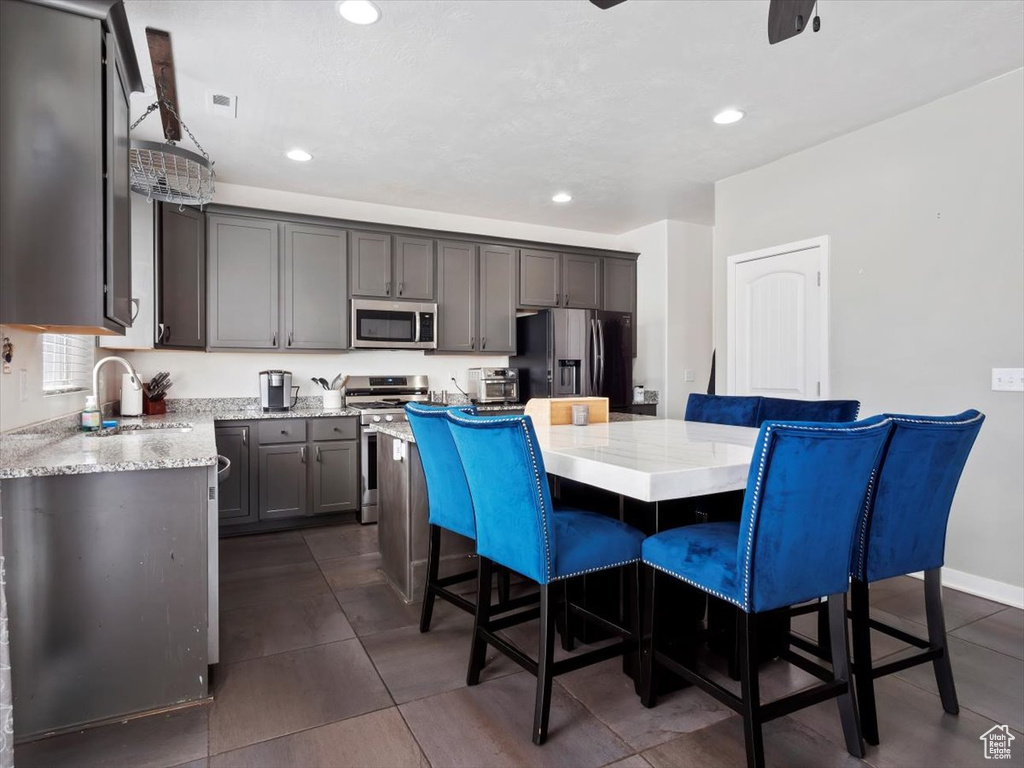 Kitchen featuring a center island, sink, dark tile flooring, stainless steel appliances, and light stone countertops