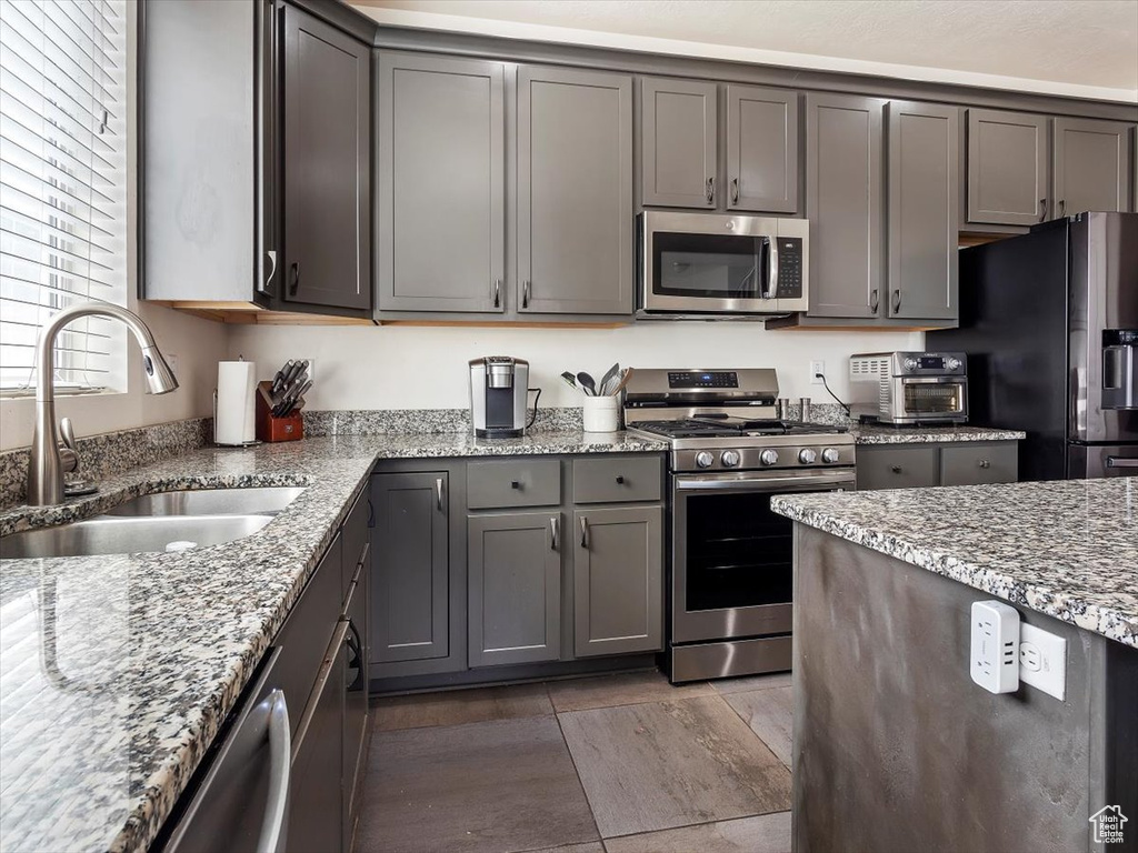 Kitchen with gray cabinets, stainless steel appliances, sink, and light stone counters