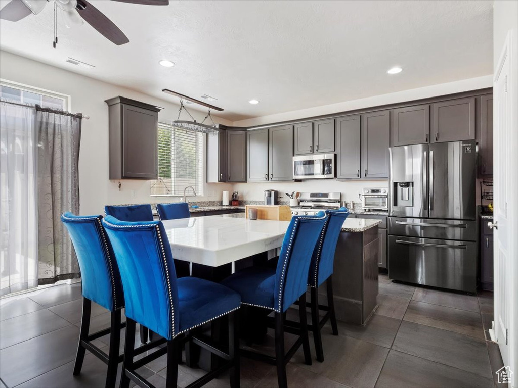 Kitchen with light stone counters, ceiling fan, a kitchen island, stainless steel appliances, and a kitchen breakfast bar