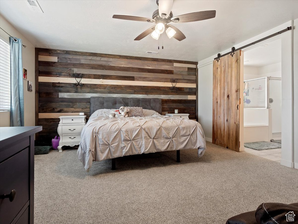 Carpeted bedroom featuring wooden walls, a barn door, and ceiling fan