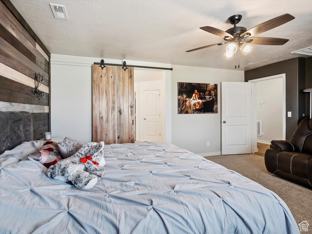 Bedroom with ceiling fan, a barn door, and carpet flooring