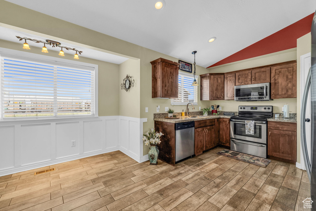 Kitchen featuring appliances with stainless steel finishes, vaulted ceiling, light stone counters, rail lighting, and sink