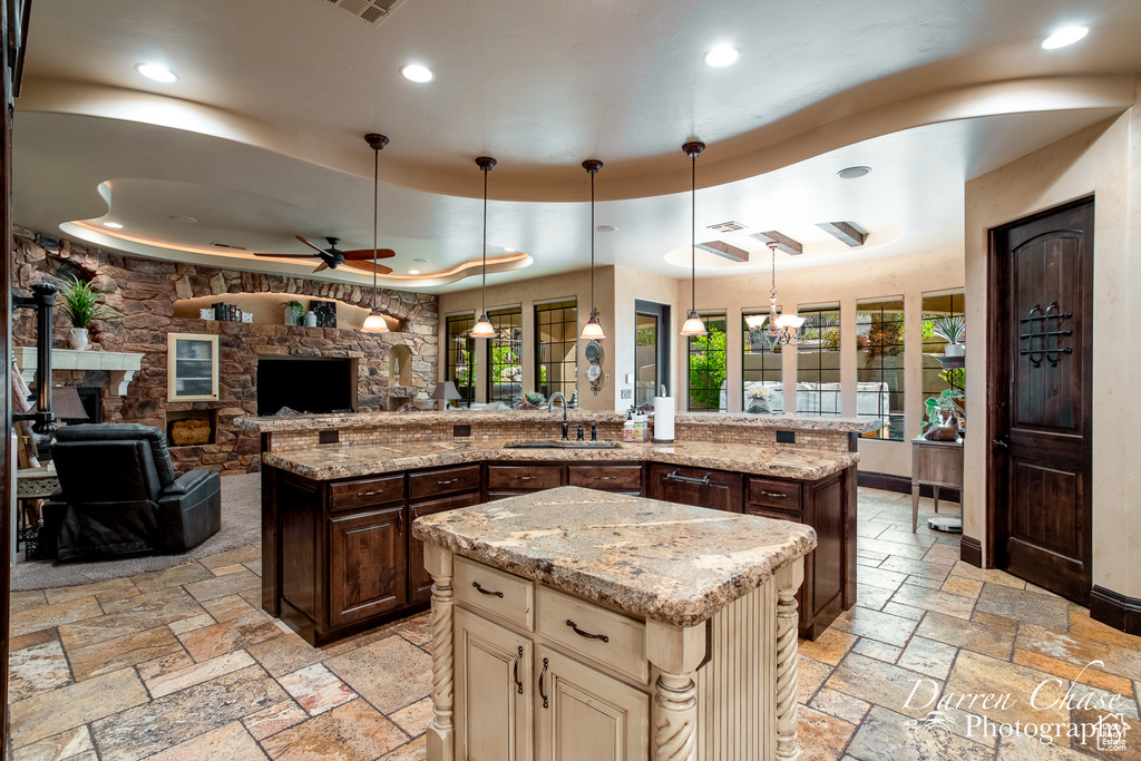 Kitchen featuring decorative light fixtures, light stone counters, ceiling fan with notable chandelier, and a kitchen island with sink