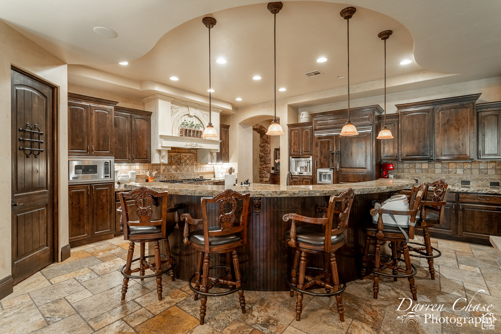 Kitchen with hanging light fixtures, stainless steel appliances, backsplash, and light tile floors