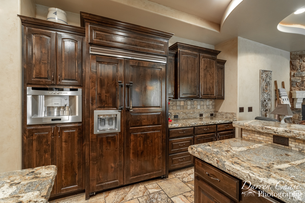 Kitchen featuring tasteful backsplash, dark brown cabinets, light tile floors, and light stone counters