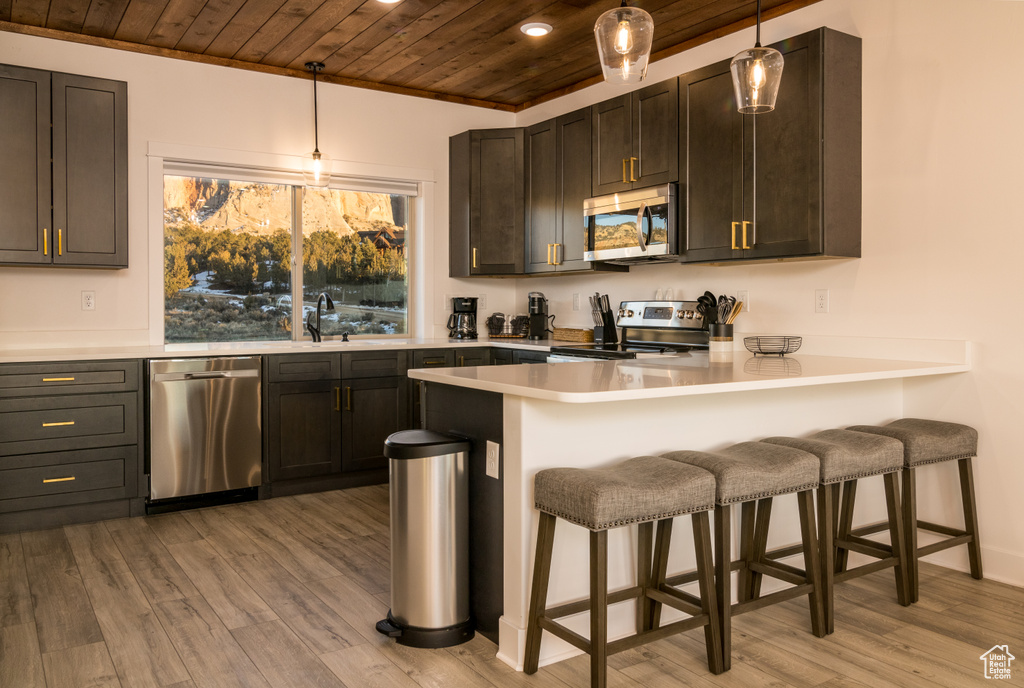 Kitchen with appliances with stainless steel finishes, light hardwood / wood-style floors, wooden ceiling, pendant lighting, and a breakfast bar