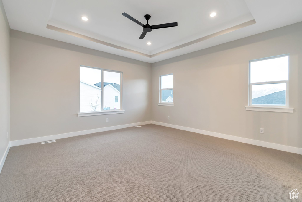 Unfurnished room with a raised ceiling, ceiling fan, and carpet flooring