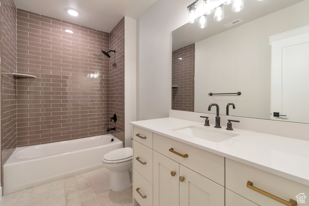 Full bathroom featuring oversized vanity, tile floors, toilet, and tiled shower / bath