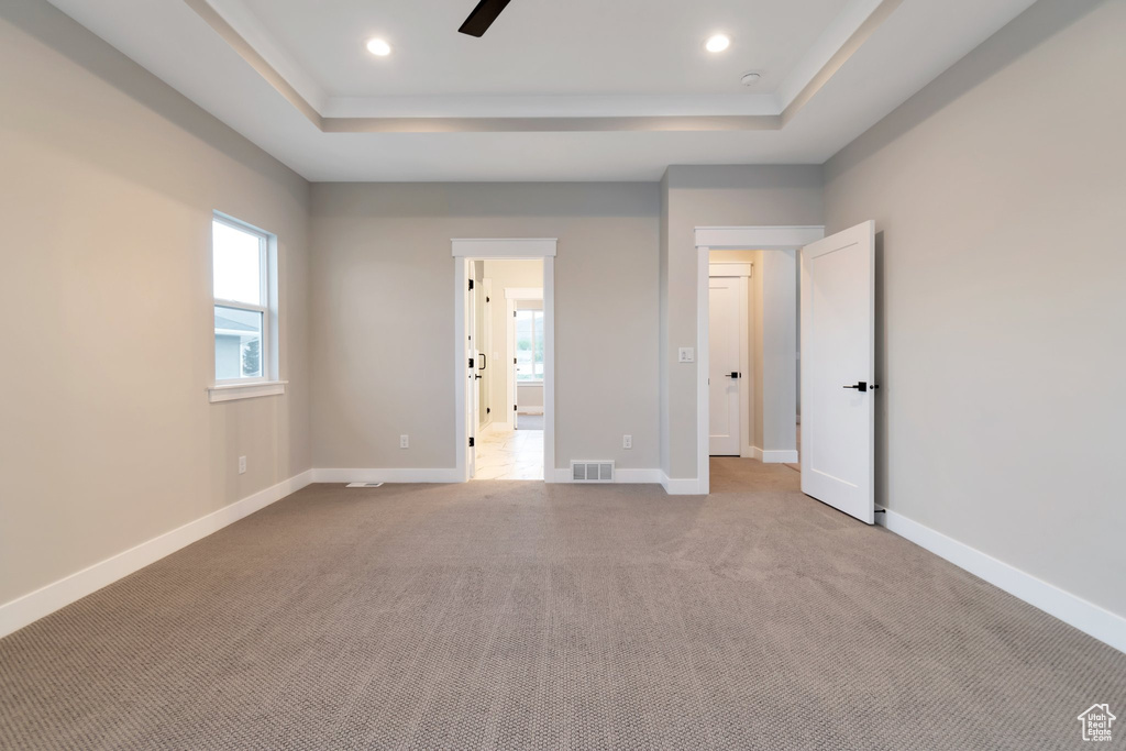 Unfurnished bedroom with carpet, ceiling fan, and a tray ceiling