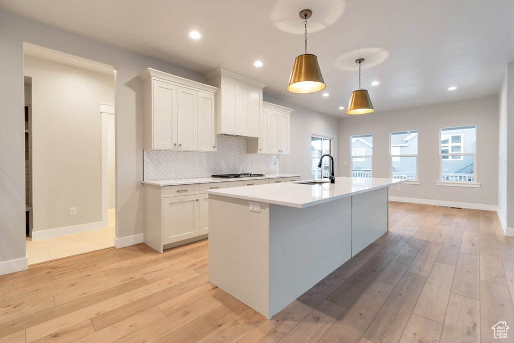 Kitchen featuring white cabinets, light hardwood / wood-style flooring, a center island with sink, and backsplash