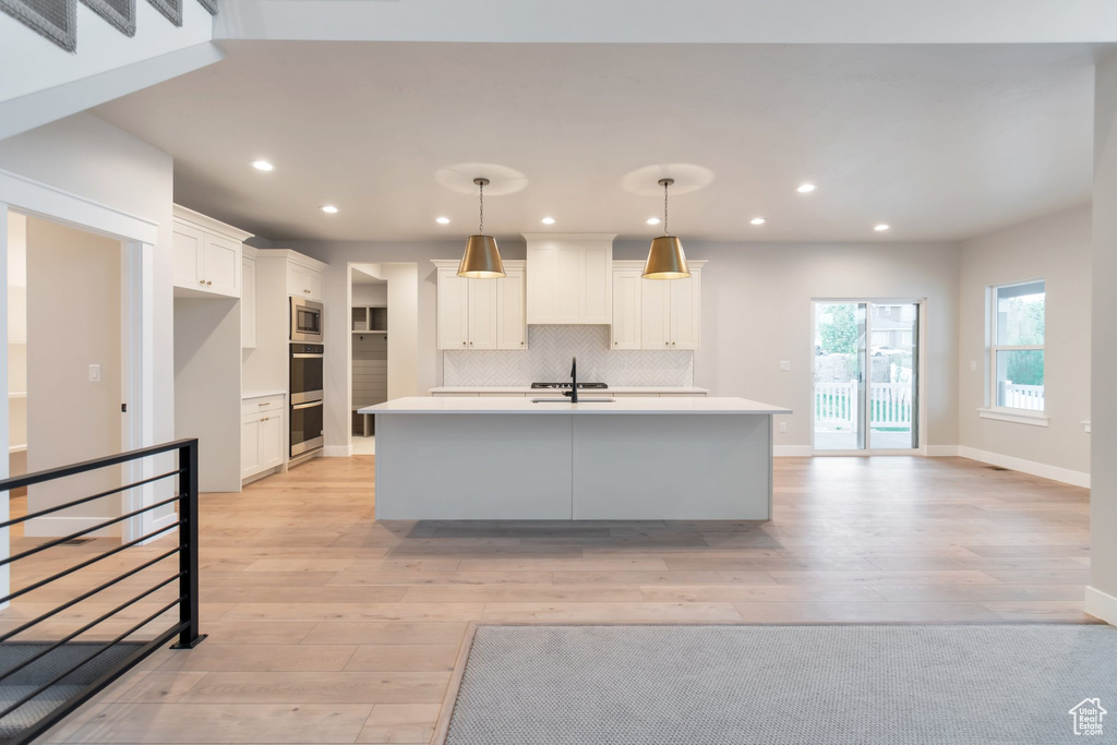 Kitchen with backsplash, a kitchen island with sink, white cabinets, sink, and light wood-type flooring