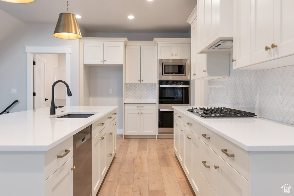Kitchen featuring premium range hood, stainless steel appliances, tasteful backsplash, an island with sink, and sink
