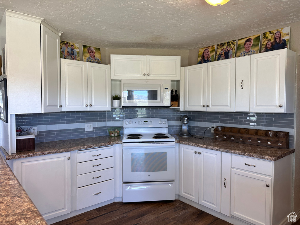 Kitchen featuring white appliances, backsplash, white cabinetry, dark stone counters, and dark wood-type flooring