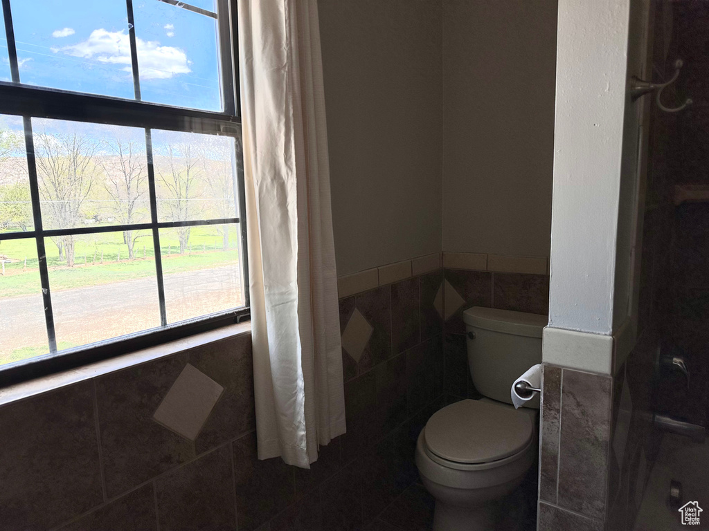 Bathroom featuring tile walls, toilet, and a wealth of natural light