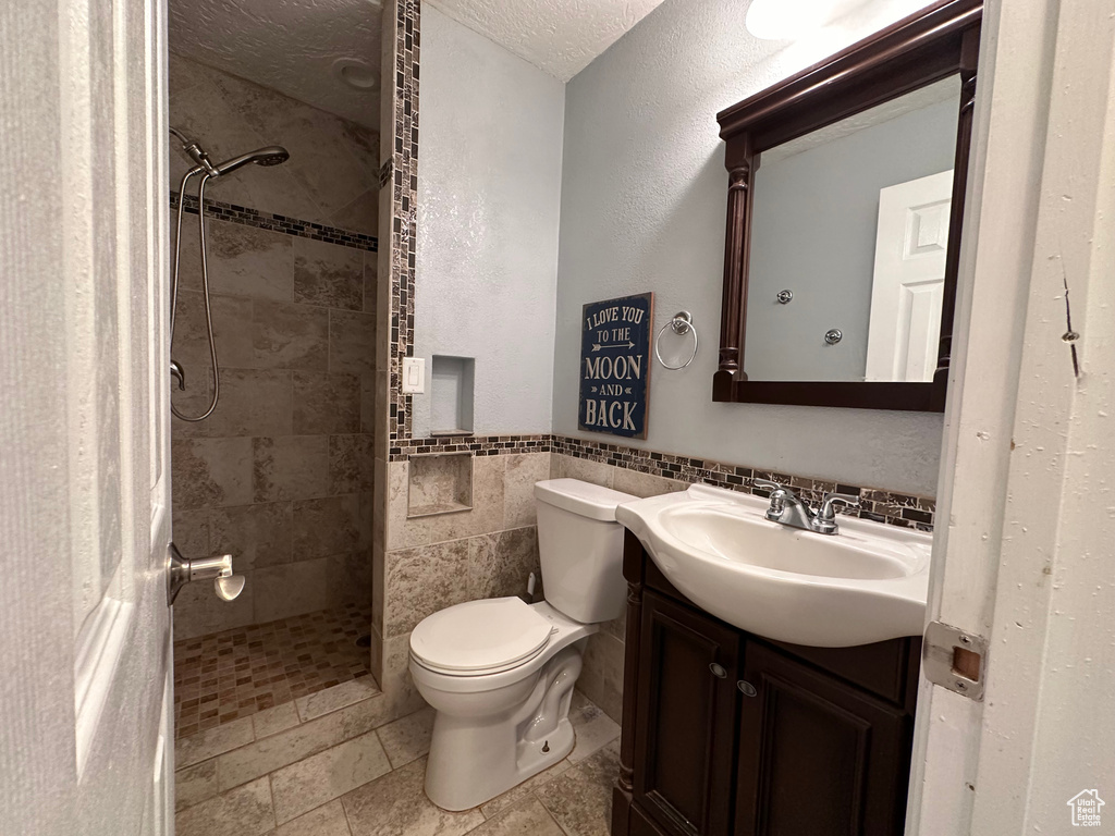 Bathroom with tile walls, vanity, a tile shower, toilet, and a textured ceiling