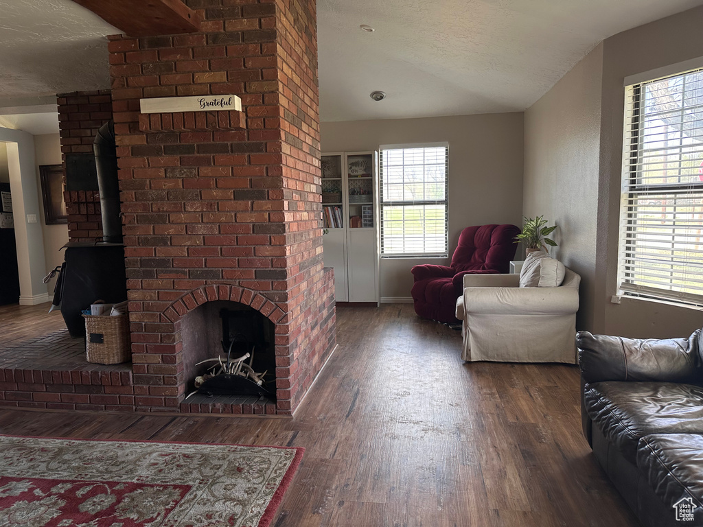 Living room featuring a wood stove, dark hardwood / wood-style floors, brick wall, a textured ceiling, and lofted ceiling