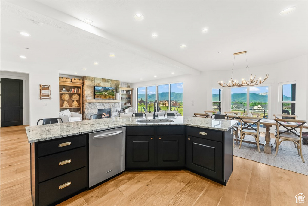 Kitchen featuring a center island with sink, stainless steel dishwasher, sink, and light wood-type flooring