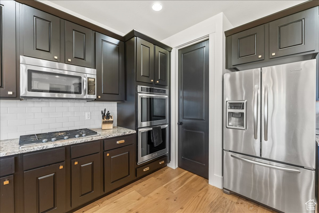 Kitchen featuring dark brown cabinets, stainless steel appliances, light stone counters, tasteful backsplash, and light hardwood / wood-style floors